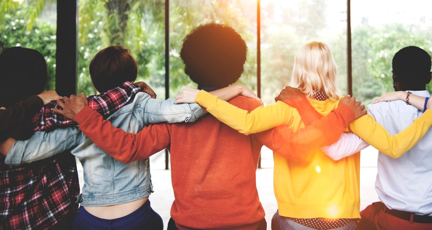 Group of happy young people linking arms and looking out at the sun.